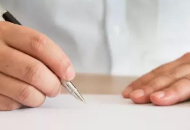Mains posées sur la table, avec un stylo. Pas d'information sur le visuel.
